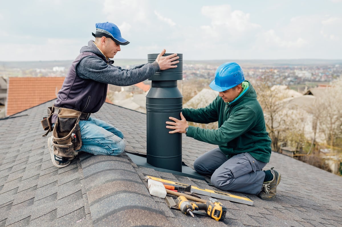 Two professional workmen standing on rooftop measuring chimney of new house under construction