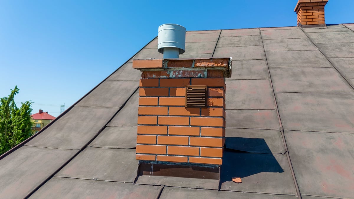 A close-up of a brick chimney on a roof against a clear blue sky